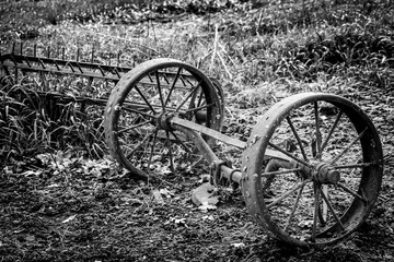 Fototapeta na wymiar Black and white old farm equipment wheels in a field.