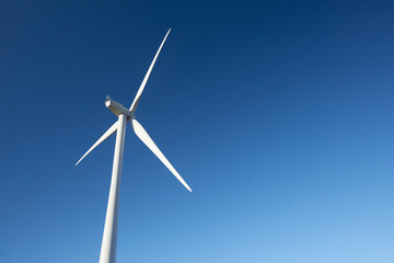 Close up of a single turbine from behind on a wind farm against a clear blue sky.