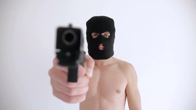 Terrorist with a naked torso in balaclava aims his gun on white background