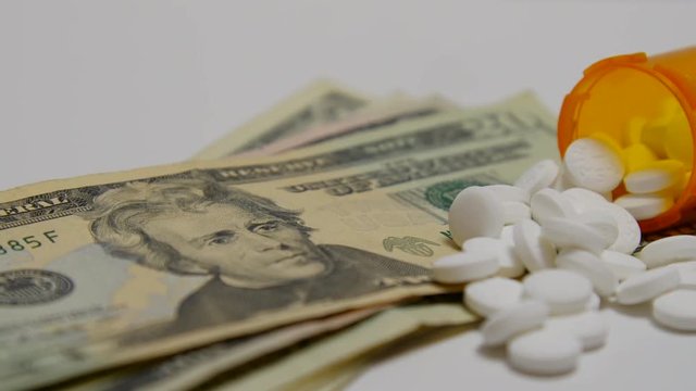 Bottle of pills spilled out onto stack of money.
