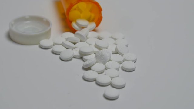 Camera pans to a bottle of pills spilling out onto white surface.