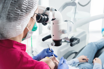 A female professional dentist examines a female patient with a stamotologic microscope in her office. Stamotologist profession concept