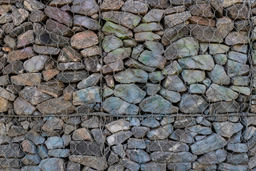 Background of stones. A wall of cobblestones, stones with metal mesh fencing