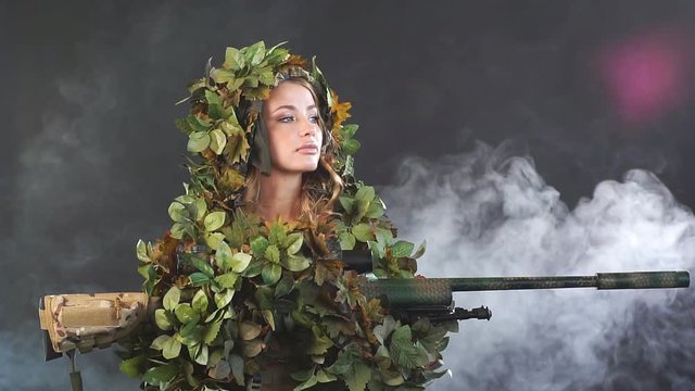 Camouflaged woman sniper in ghillie suit posing with rifle in foggy night. Slow motion. Special Weapons and Woman Concept.