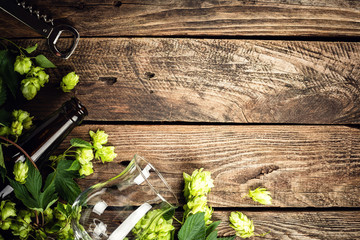 beer background of empty beer glass, bottle and fresh hops on an old wooden table. top view. space...