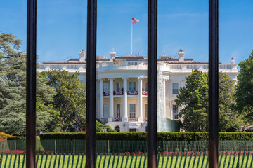 The White House behind the bars of the fence at sunny day in Washington DC.