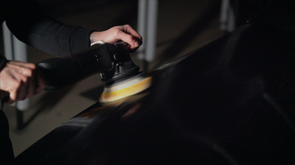 Car detailing - Hands with orbital polisher in auto repair shop. Selective focus. Car polishing and LCP correction