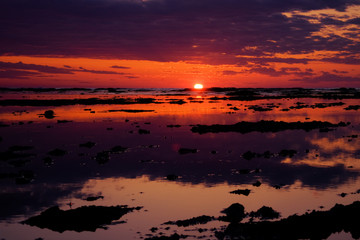 Fototapeta na wymiar Beautiful red sunset. The sun is setting in the sea. Reflection in the sea, rocky shore. Sun rays.