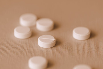 White tablets scattered on a surface close up. Brown color toned