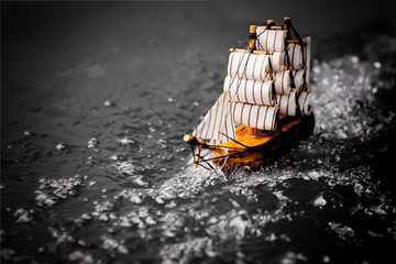 small toy boat in the water with big waves, black and white.