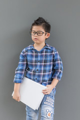 Asian boy ready to go to school and his hands hold the book against the gray wall
