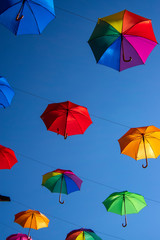 Fototapeta na wymiar Group of umbrellas hanging on a rope isolated against blue background, wallpaper background, bright various colors scenery