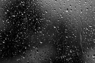 Raindrops on glass in rainy weather close up. Natural background black and white