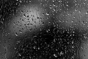 Raindrops on glass in rainy weather close up. Natural background black and white