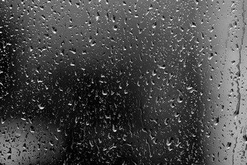Raindrops on glass in rainy weather close up. Natural background black and white