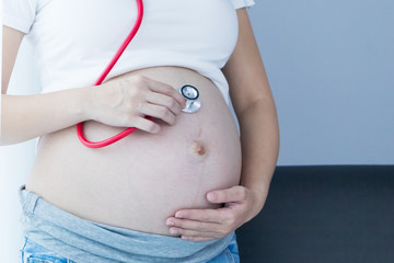 Portrait of Beautiful young pregnant women using stethoscope listening to her tummy.Pregnancy health care preparing for baby concept.Motherhood among teenage mother.