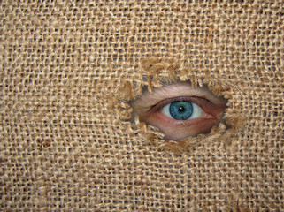 The man's eye looks through a hole in the torn sack. Burlap background.