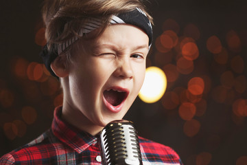 Cute little boy with microphone singing against dark background