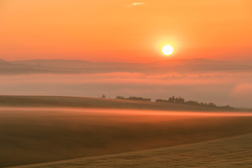 Fototapeta premium Landscape of the colorful sunrise over the foggy hills and fields