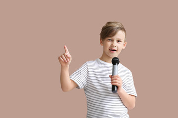 Cute little boy with microphone singing against color background