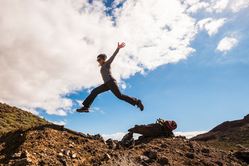 People in outdoor leisure activity - cheerful happy woman jumping on the rocks during hiking and trekking sport active lifestyle - mountains and blue sky in background - freedom and joy concept