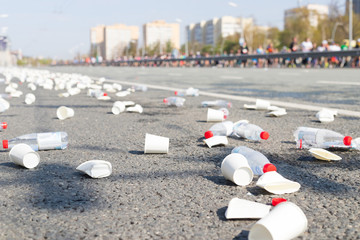 A bunch of plastic cups and empty bottles on the road while a marathon running