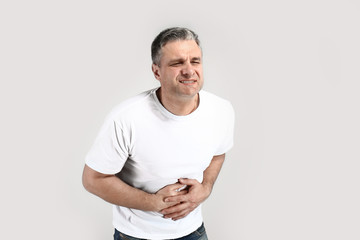Handsome mature man suffering from stomach pain on grey background