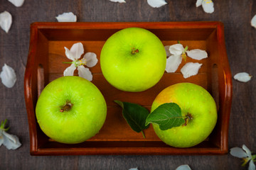 Green apples, flowers and leaves on a wooden tray. Still life with fruit on a wooden table.