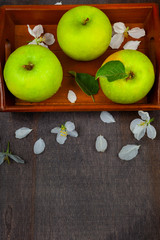 Green apples, flowers and leaves on a wooden tray. Still life with fruit on a wooden table.