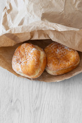 Jam doughnuts in a brown paper bag,  recycling packaging,  on a grey wood background