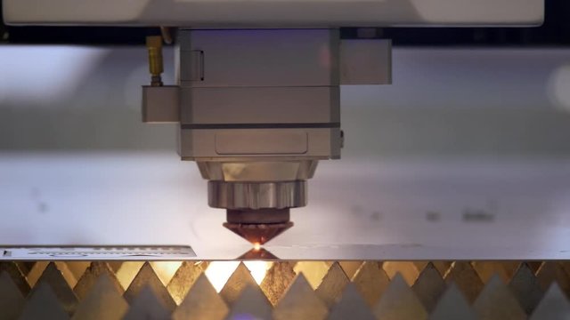 Cutting of metal. Sparks fly from laser. Industrial laser cutter with sparks. The programmed robot head cuts with the aid of a huge sheet of metal temperature