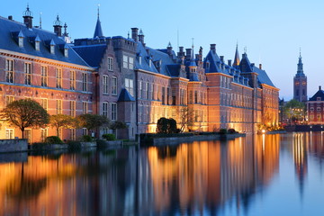 Reflections of the Binnenhof (13 century gothic castle) on the Hofvijver lake at dusk during the blue hour, with the clock tower of Grote of Sint Jacobskerk on the right, The Hague, Netherlands - obrazy, fototapety, plakaty