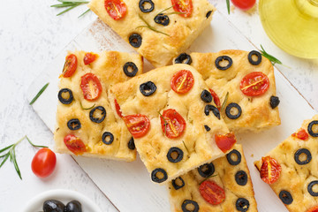 Sliced pieces of focaccia with tomatoes, olives and rosemary. Traditional Italian flat bread. Top view.