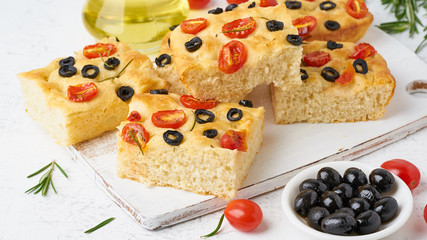 Focaccia with tomatoes, olives and rosemary, side view, close up. Traditional Italian flat bread