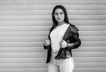 Girl wearing t-shirt with place for logo, glasses and leather jacket posing against street