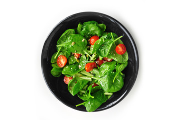 Salad in a black plate of juicy spinach leaves, cherry tomatoes and olive oil