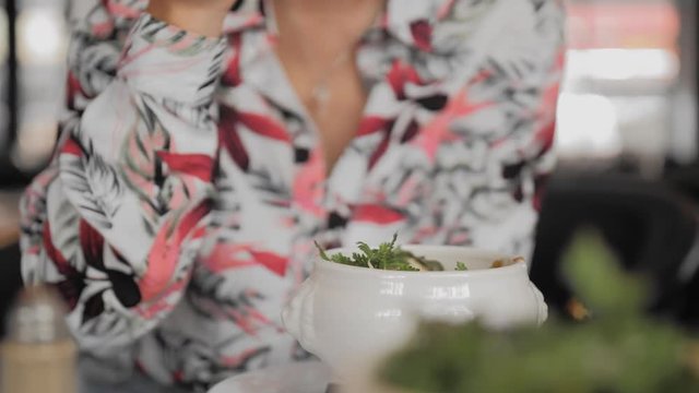 Unrecognized female tourist in a colorful shirt spoon eats a traditional French onion soup with croutons, melted cheese and herbs in a Paris restaurant. Close-up, Slow Motion.