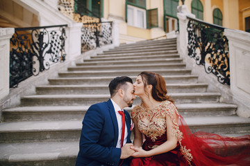 Beautiful woman in a long red dress walks around the city with her husband in a blue suit and with a beard