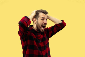 Half-length close up portrait of young man in shirt on yellow background. The human emotions, facial expression concept. Trendy colors. Astonished and crazy screaming while holding his head.