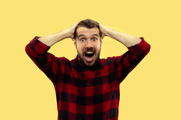 Half-length close up portrait of young man in shirt on yellow background. The human emotions, facial expression concept. Trendy colors. Astonished and crazy screaming while holding his head.