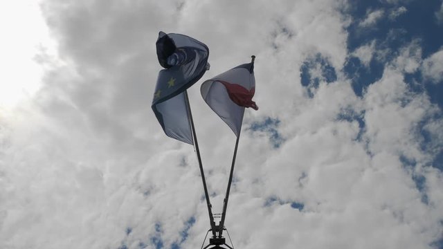 Symmetrically located Flag of France and European Union waves in the wind on the flagpole. Against the background of blue sky with rare clouds. Slow Motion.