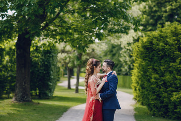 Fototapeta premium Beautiful woman in a long red dress walks around the city with her husband in a blue suit and with a beard