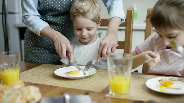 mother cut the scruble eggs for son during the family dinner