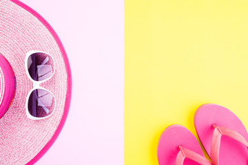 Beach accessories sunglasses, flip flop starfish beach hat and sea shell on pink and yellow background for summer holiday and vacation concept.