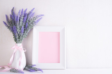 White picture frame with lovely purple flower in vase on white wooden table.