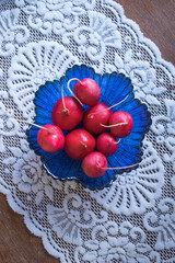 Fresh ripe radishes in a blue glass salad bowl on a wooden table with beautiful white tablecloth. Top view