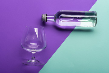 transparent wineglass and bottle with water on bright purple and azure background  