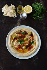 Fresh hummus with olives, paprika and parsley on a plate.