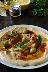 Fresh hummus with olives, paprika and parsley on a plate.