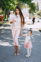 Young and very beautiful slim mum with long hair walking in a sunny summer city with her little beauties daughters